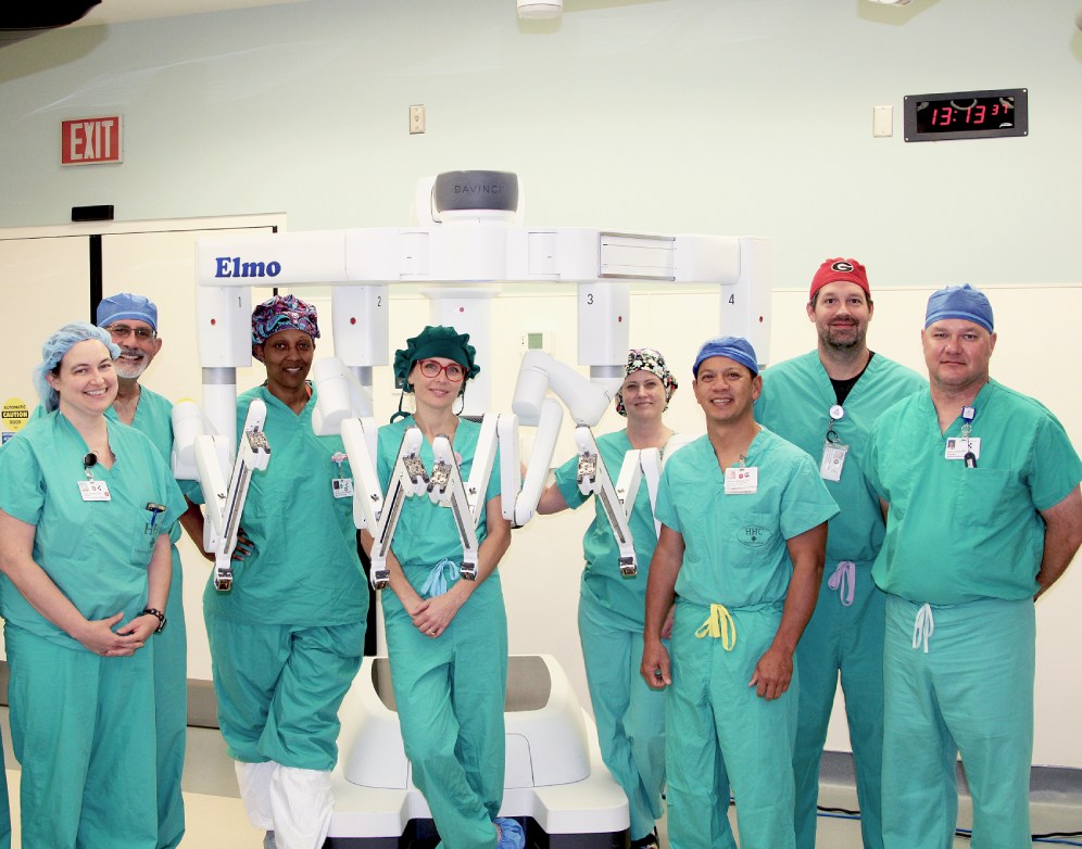 a group of surgeons in green scrubs standing around the elmo robotic surgery machine